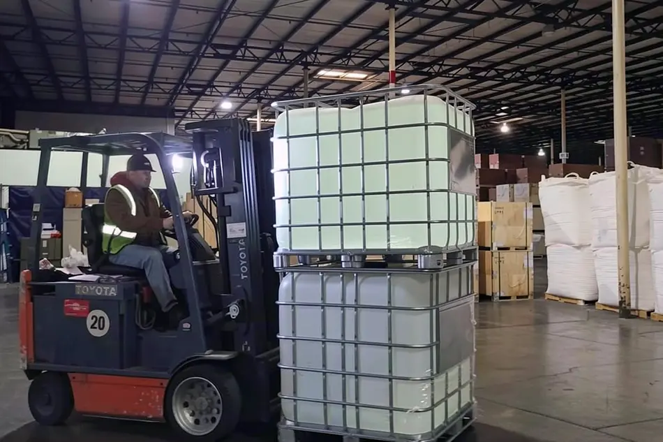 Forklift driver moving caged IBC totes as part of chemical handling services